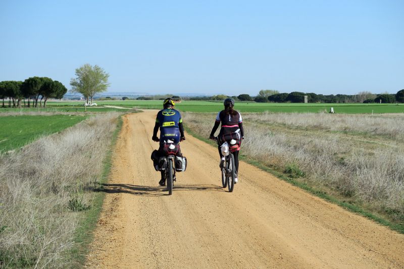 Pareja de bicigrinos avanzando a buen ritmo por una pista de tierra.