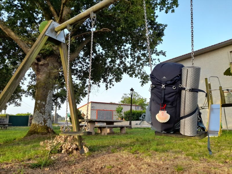Foto de una mochila de peregrino en un columpio cerca de un albergue.